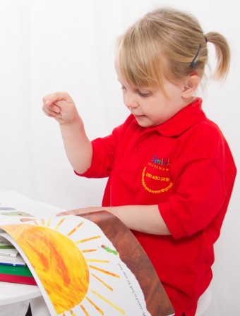 Little girl wearing a red polo shirt while reading a book